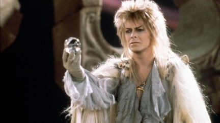 Jareth (David Bowie) holds up a glass orb, wearing a shimmery silver outfit and heavy makeup.