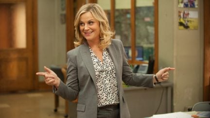 Leslie Knope smiling and making finger guns pointing off camera in Parks and Recreation.