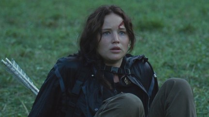 Katniss sitting on the ground in The Hunger Games.