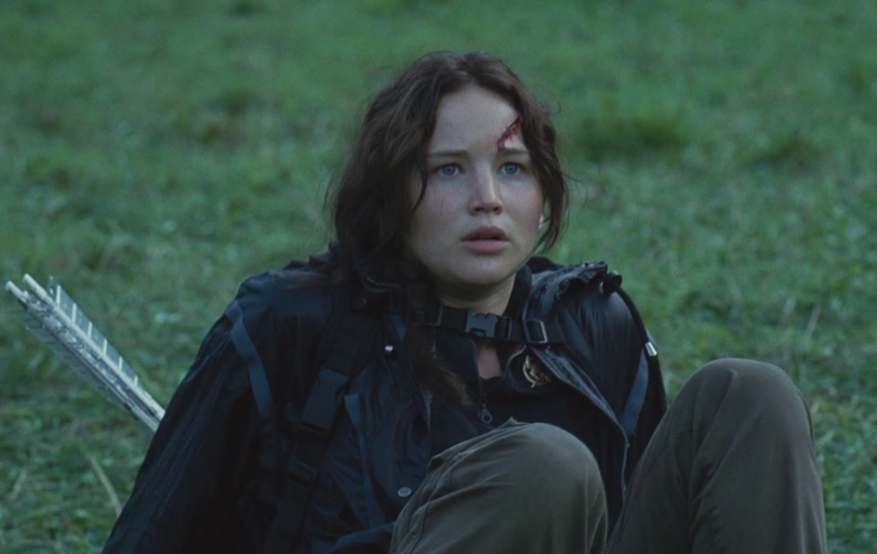 Katniss sitting on the ground in The Hunger Games.