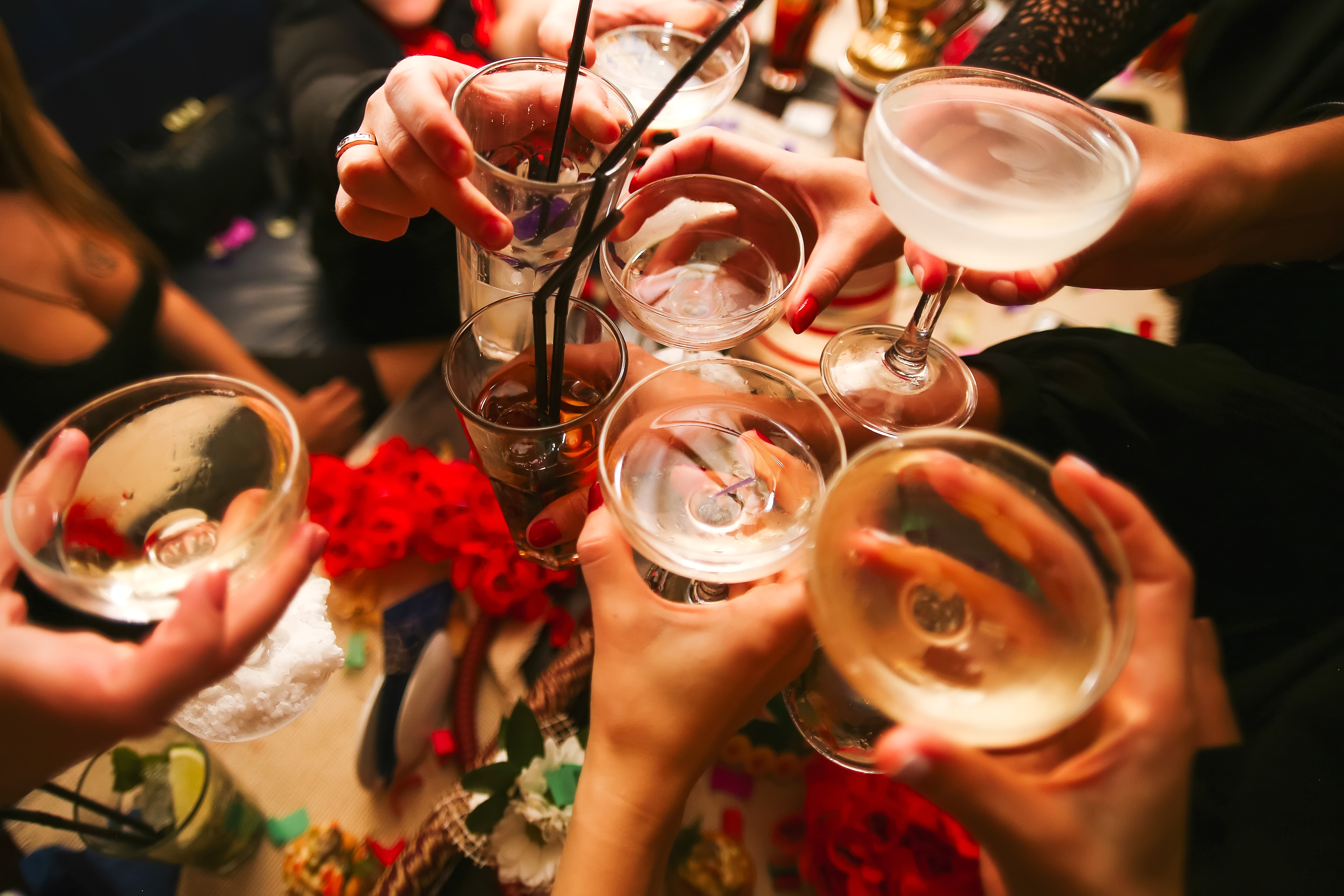 A group of people clinking various glasses in a toast, close-up of hands and glassware at a celebration
