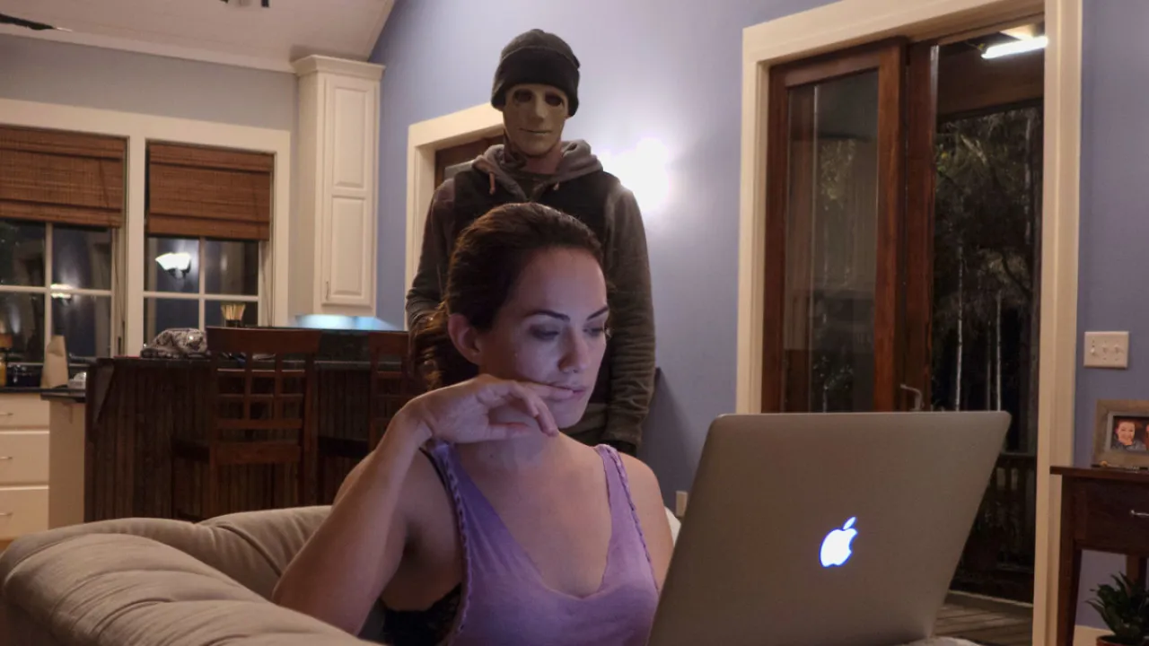 A woman stares at her laptop while a masked intruder hovers in the background in 'Hush'