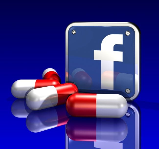 3d illustration of a large blue Facebook logo standing upright behind three large red and white pills on a blue reflective surface
