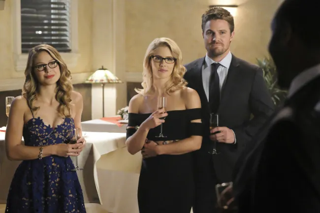 image: Bettina Strauss/The CW Supergirl -- "Crisis on Earth-X, Part 1" -- Pictured (L-R): Melissa Benoist as Kara, Emily Bett Rickards as Felicity Smoak and Stephen Amell as Oliver Queen -© 2017 The CW Network, LLC. All Rights Reserved