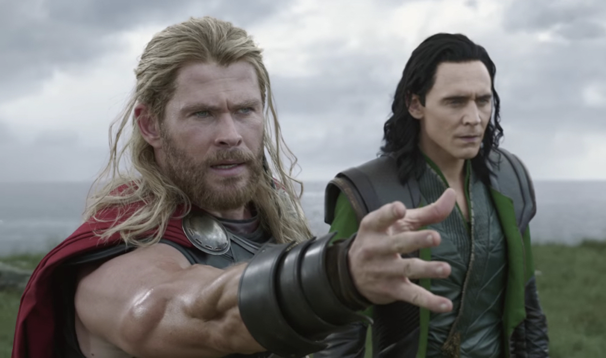 Thor (Chris Hemsworth) and Loki (Tom Hiddleston) stand beside each other as Thor summons his hammer.