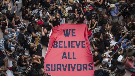 A crowd of people protesting Brett Kavanaugh's confirmation hold a sign reading 'We believe all survivors'