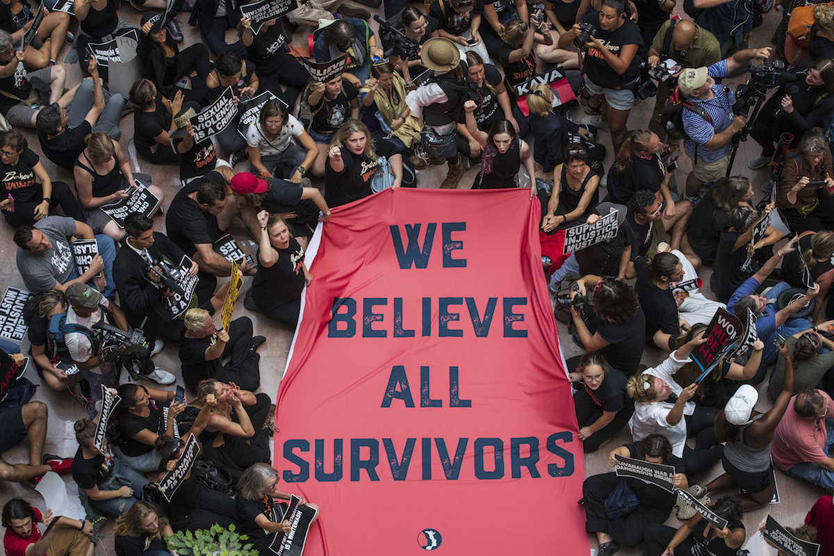A crowd of people protesting Brett Kavanaugh's confirmation hold a sign reading 'We believe all survivors'