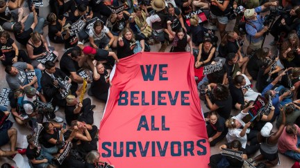 A crowd of people protesting Brett Kavanaugh's confirmation hold a sign reading 'We believe all survivors'