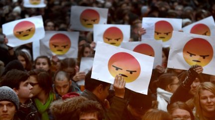 Protestors hold up signs with Facebook's angry face reaction on them.
