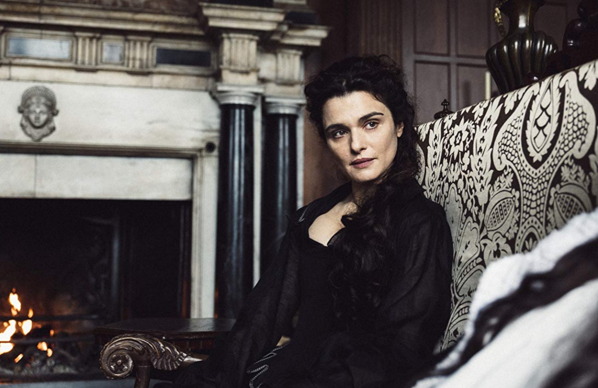 Rachel Weisz sitting on a couch with a stern look in "The Favourite"