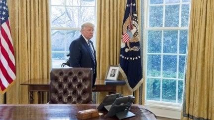 Donald Trump looks very small standing behind his desk in the Oval Office.
