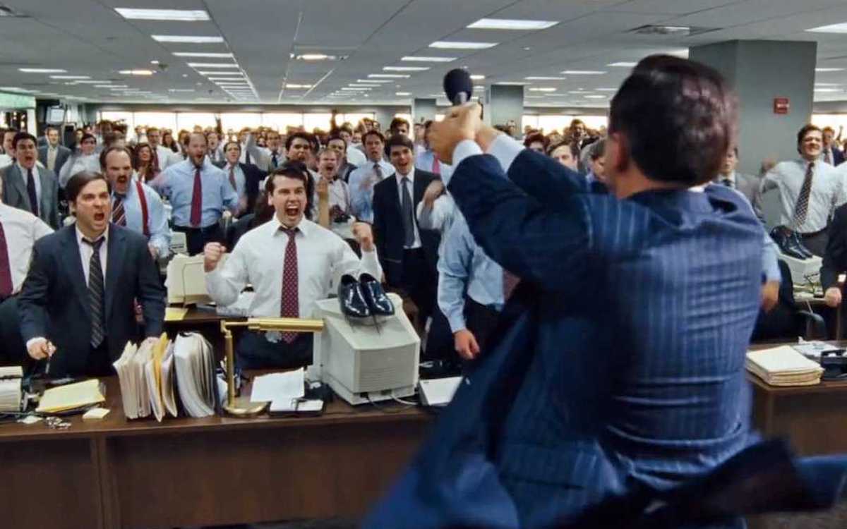 Leonardo DiCaprio holds a phone up to a room of men in The Wolf of Wall Street.