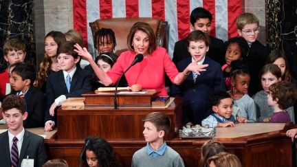 Nancy Pelosi stands at her podium, surrounded by children of representatives.
