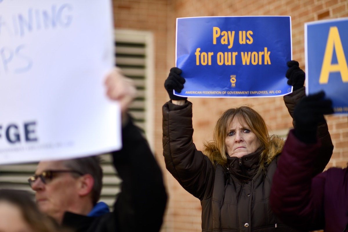 Furloughed female TSA employee holds a sign reading 'Pay us for our work'