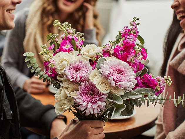 Man holding a bouquet of flowers talking to women.