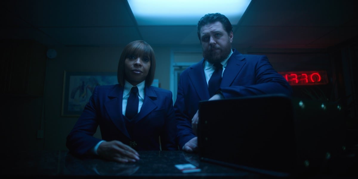 Mary J. Blige and Cameron Britton standing together wearing suits.