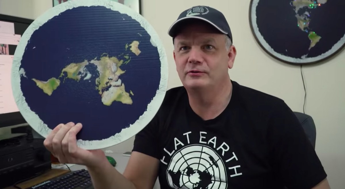mark sargent holding up a round image of a flat Earth in behind the curve