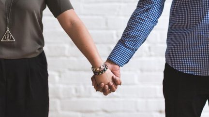 Cropped torsos of man and woman holding hands.