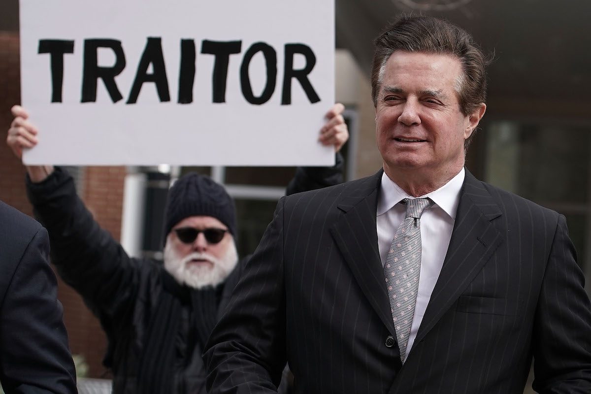 Paul Manafort followed by a protestor with a sign accurately reading 'Traitor.'