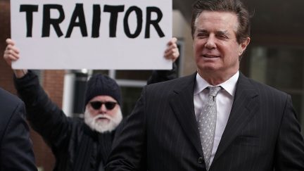 Paul Manafort followed by a protestor with a sign accurately reading 'Traitor.'