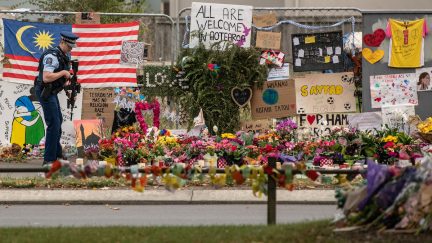An armed police officer pauses by flowers and tributes near Al Noor mosque