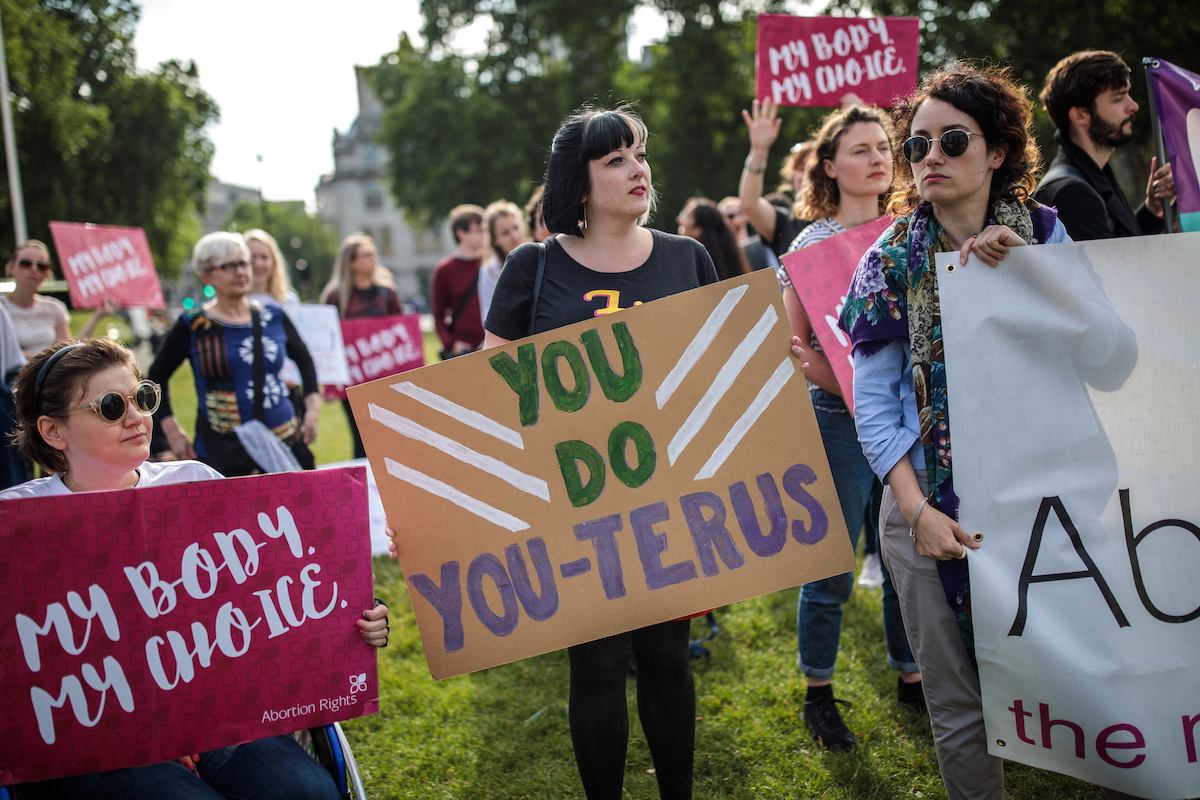 Pro-choice protestors holding signs. One reads "you do you-terus."