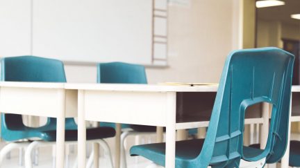 Empty school chairs around a desk.
