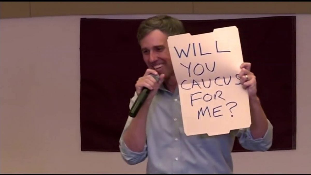 Beto O'Rourke holds up a sign asking a girl in the audience "Will you caucus for me?"