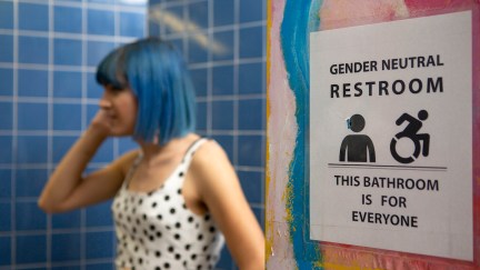 A nonbinary femme with blue hair in a gender-neutral bathroom.