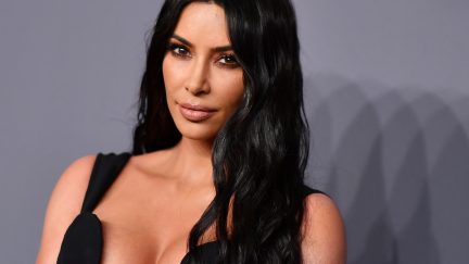 Kim Kardashian in a low-cut black dress on a red carpet.