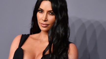 Kim Kardashian in a low-cut black dress on a red carpet.