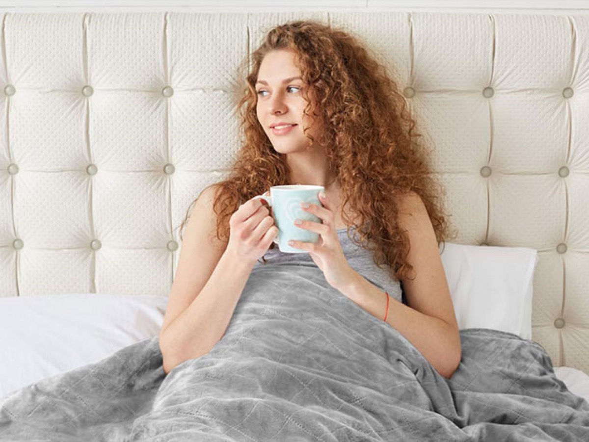 A woman drinking from a mug in bed, as you do.