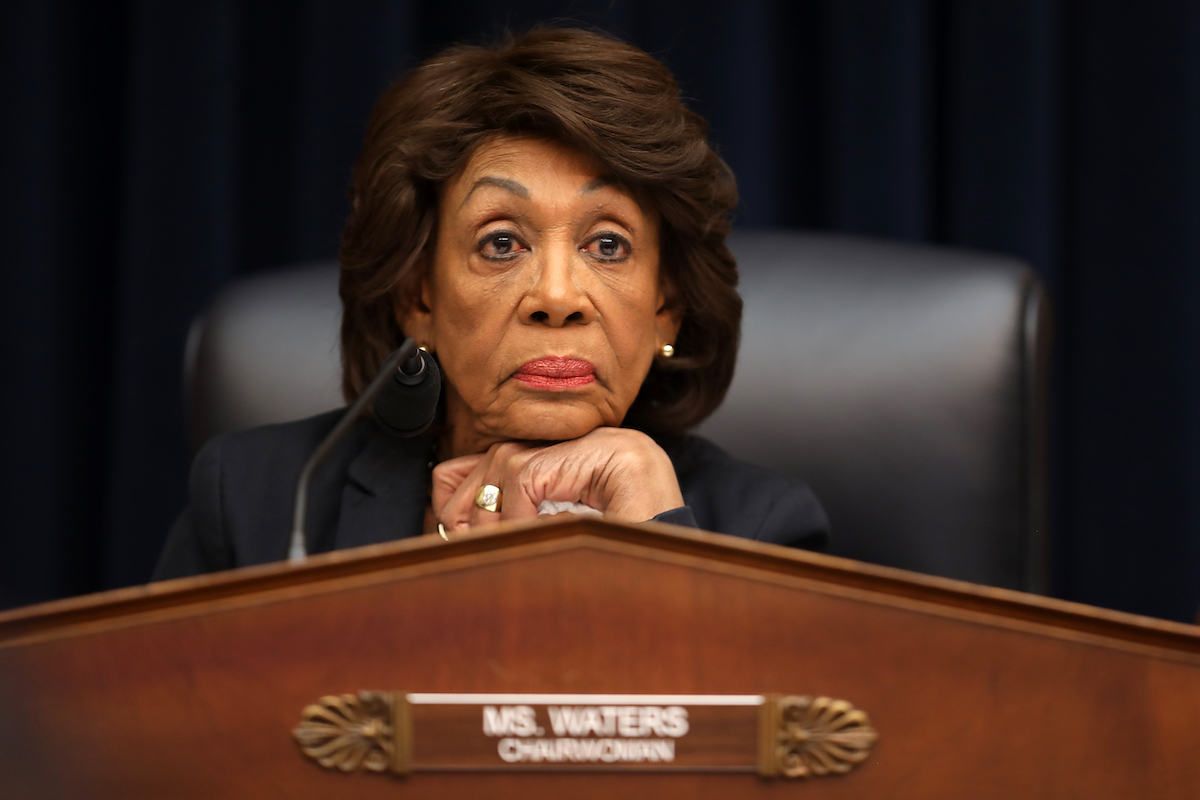 Congresswoman Maxine Waters rests her head on her chin, fresh out of patience, above a plaque reading Chairwoman.