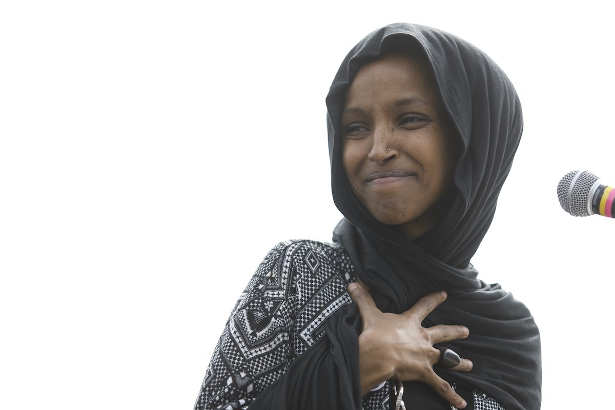 Rep. Ilhan Omar stands in front of a microphone, beaming during a climate change rally.