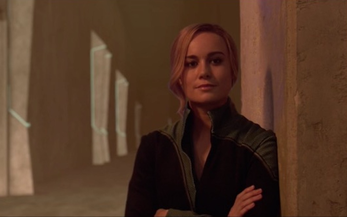 Carol Danvers leans against a wall and smirks.