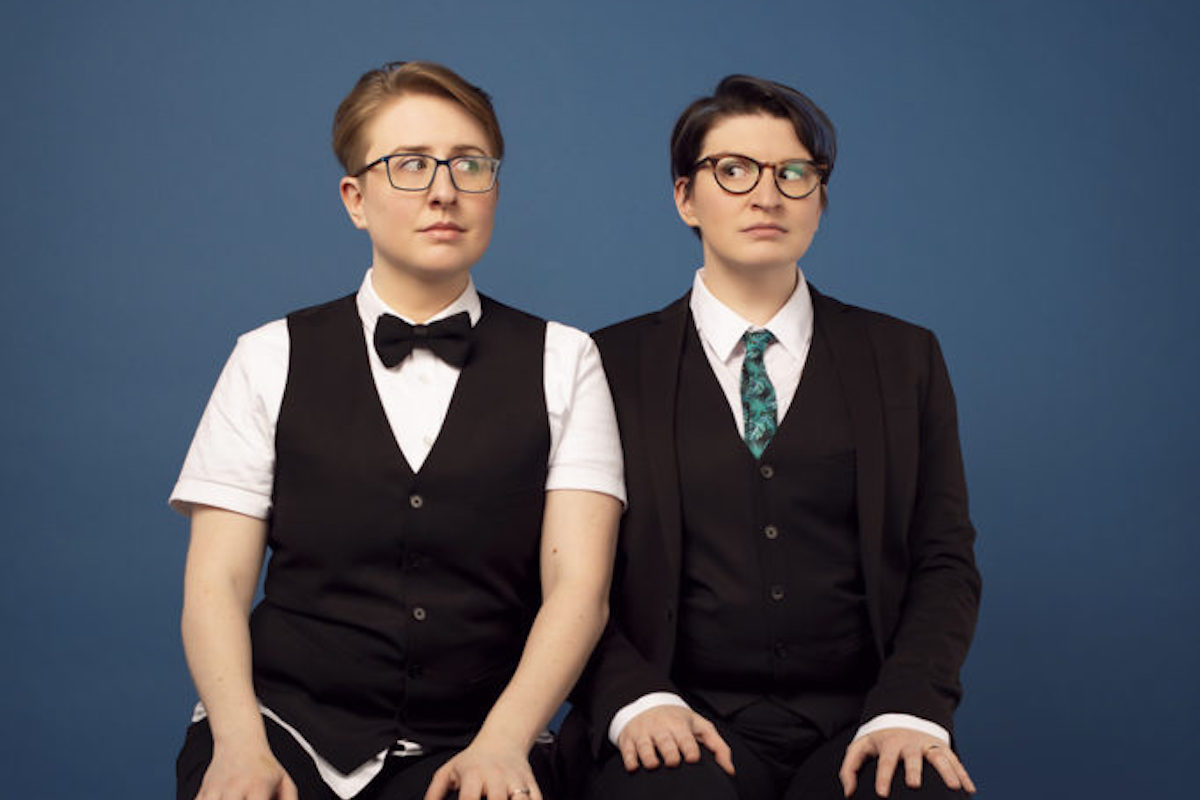 ser Malena-Webber and Aubrey Turner of The Doubleclicks sit side by side in suits.