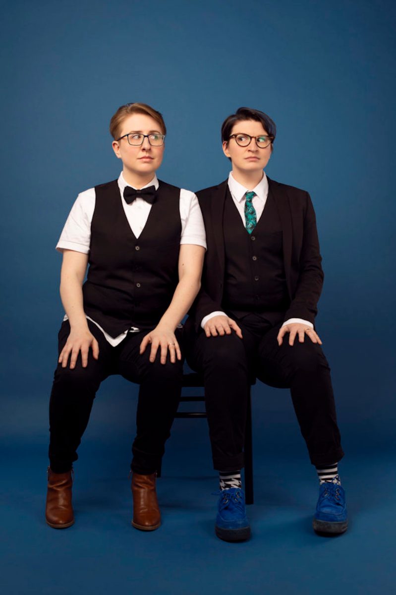 ser Malena-Webber and Aubrey Turner of The Doubleclicks sit side by side in suits.