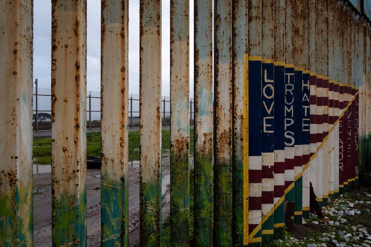 Picture of a section of the US-Mexico border fence with a mural painted on it reading 'Love Trumps Hate.'