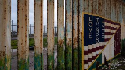 Picture of a section of the US-Mexico border fence with a mural painted on it reading 'Love Trumps Hate.'