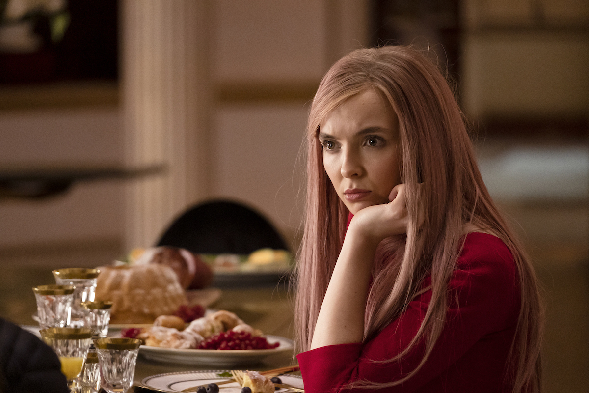 Villanelle (Jodie Comer) rests her chin in her hand, looking like she has questions too.