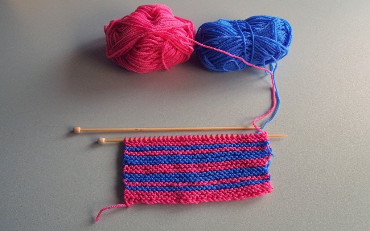 Pink and blue yarns being knit into stripes.