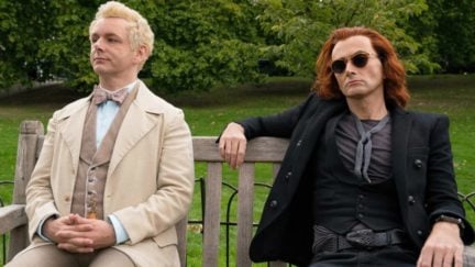 Aziraphale and Crowley sit on a bench, looking kind of bored in Amazon Prime's Good Omens.