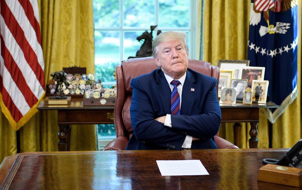 Donald Trump crosses his arms and looks pouty behind his Oval Office desk.