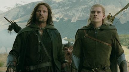 Aragorn (Viggo Mortensen) a man with a beard and a sword and Legolas (Orlando Bloom) an elf with long blonde hair stare off into the distance in in 'The Lord of the Rings'.
