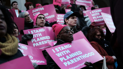 Protestors hold signs reading 