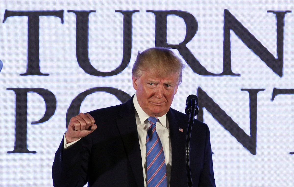 Trump pumps a fist in front of a large Turning Point sign.