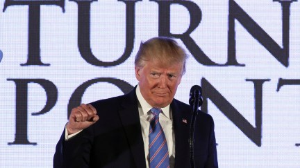 Trump pumps a fist in front of a large Turning Point sign.