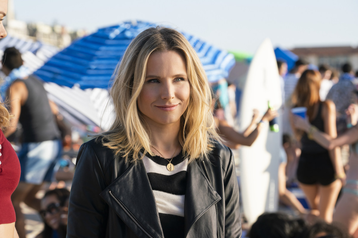 Veronica Mars (Kristen Bell) stands on a crowded beach in a leather jacket.