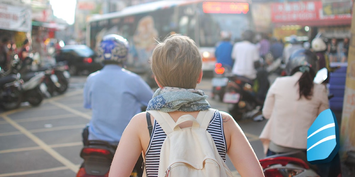 A woman wearing a backpack, walking through a crowded city.