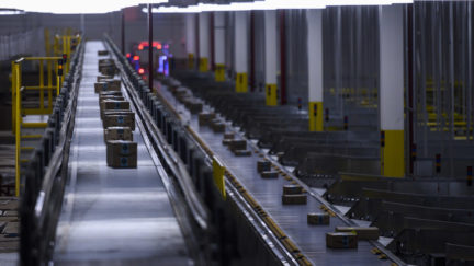 Amazon packages on a conveyor belt in a factory room.
